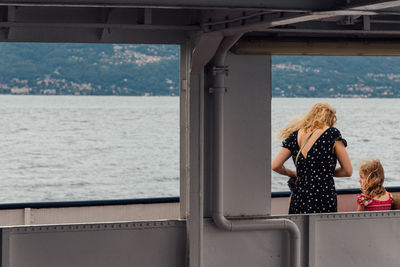 Rear view of mother and daughter standing on ferry boat in sea