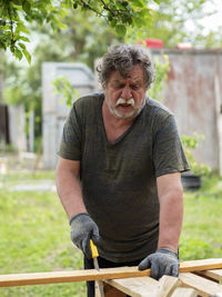 Mature caucasian man sawing a pine board in the garden