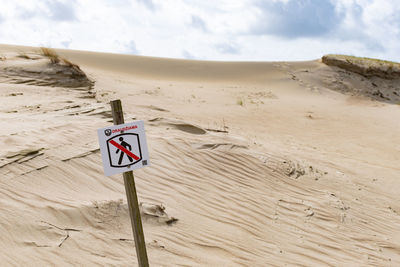 Sign board on sand at beach against sky