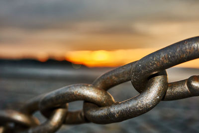 Close-up of rusty chain against sky during sunset