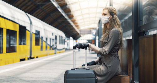 Side view of woman wearing mask sitting at railroad station