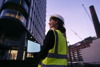 Smiling young engineer holding laptop at dusk