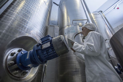 Lab technician in pharmaceutical plant in front of tanks