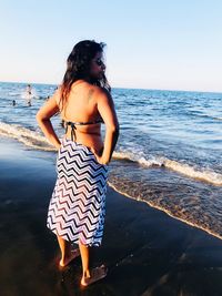 Young woman standing at beach against sky