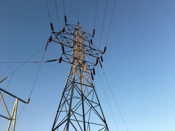 Low angle view of electricity pylon against clear blue sky