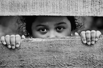 Portrait of girl looking through wooden fence