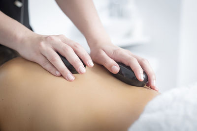 Midsection of masseuse giving lastone therapy to woman at spa