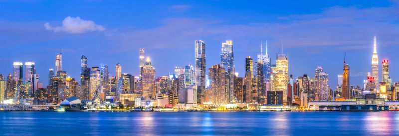 Panoramic view of illuminated buildings by sea against sky