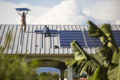 Two men install sustainable solar panels in rows on roof top.