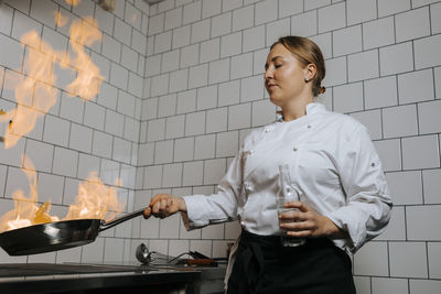 Low angle view of young female chef cooking with flambe technique in kitchen at restaurant