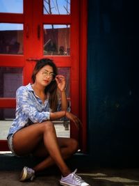 Portrait of young woman sitting against door