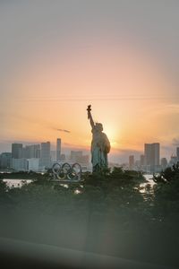 Silhouette statue against buildings in city during sunset