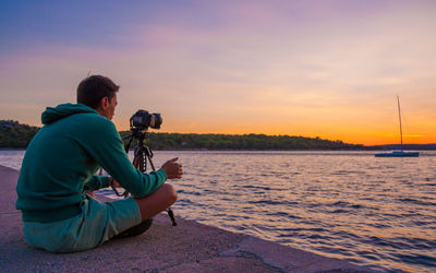 Man photographing at sea against sky during sunset