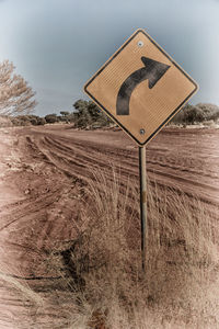 Road sign on field against sky