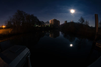 Illuminated city by river against sky at night