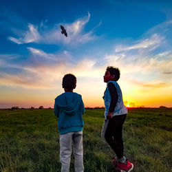 Rear view of people on field against sky during sunset