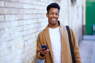 Young man using phone while standing against wall