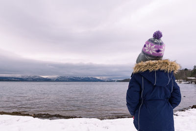 Rear view of woman standing on snow while looking at lake against sky