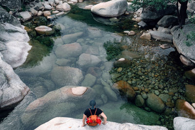 From above of anonymous male traveler with backpack sitting on rock and enjoying picturesque view of river in highland area