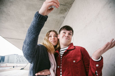 Friends making face while taking selfie against wall