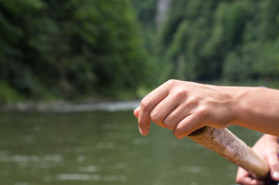 Close-up of hand holding leaf against lake