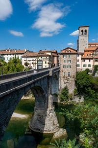 Arch bridge over river amidst buildings against sky