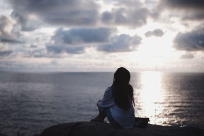 Woman sitting by sea against sky