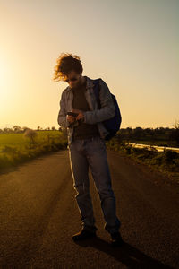 Full length of man standing on road against sky during sunset