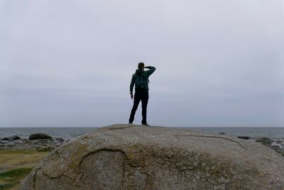 Rear view of man standing on rock against sea during sunset