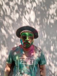 Portrait of man with powder paint on face standing against wall