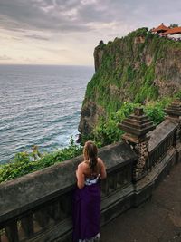 High angle view of woman looking at sea while standing by retaining wall during sunset