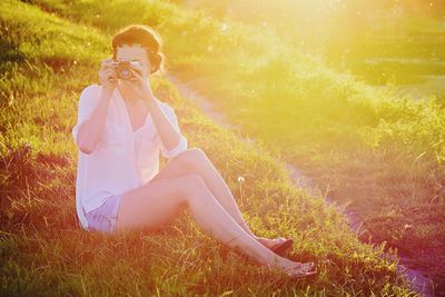 Young woman sitting on grass taking a photograp