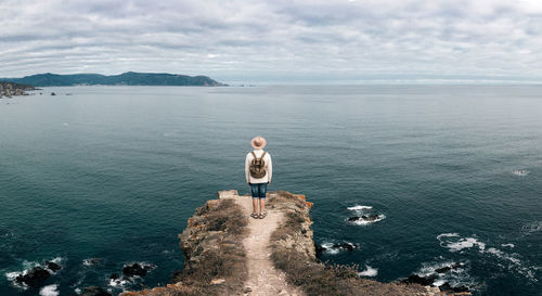 Unrecognizable male traveler standing on rocky hill and observing wonderful scenery of sea under cloudy sky