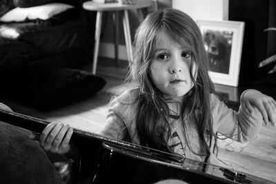 Portrait of cute girl holding guitar while sitting on floor