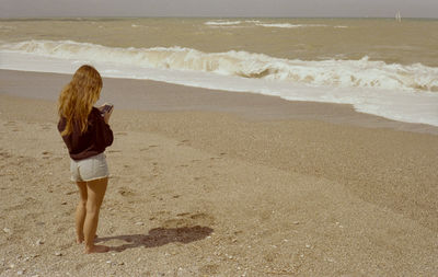 Rear view of woman photographing on beach