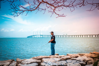 Man standing on rock by sea against sky