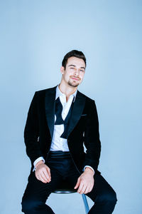 Portrait of businessman sitting on stool against blue background