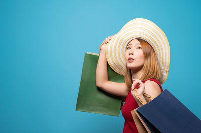 Young woman looking away while standing against blue background