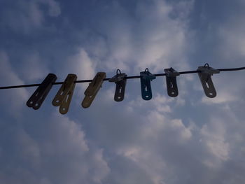 Low angle view of clothespins hanging on rope against sky