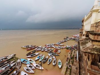 Boats moored in ganges river by temple against cloudy sky