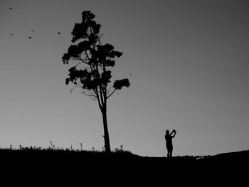 Silhouette man photographing on field against clear sky