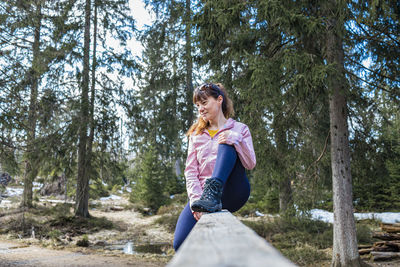 A young beautiful girl sits on a log in the forest and enjoys nature and loneliness.