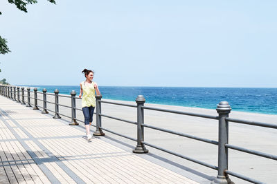 Slim woman running on the promenade with the beach and blue sea in background. strengthening. 