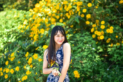 Portrait of smiling young woman standing against yellow flowering plants