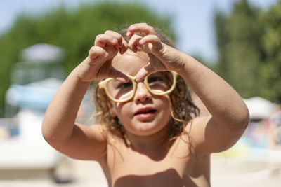 Adorable little blonde girl wearing adult glasses showing heart sign with hands at a resort
