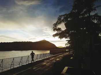 Silhouette man by railing against sky during sunset