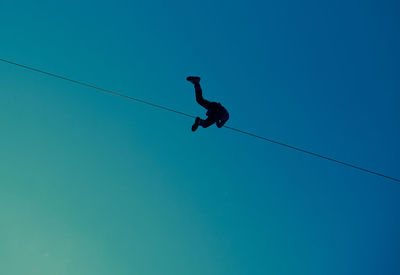 Low angle view of person performing tightrope walking against clear blue sky