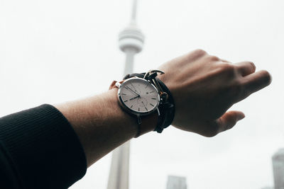 Close-up of hand holding clock against the sky