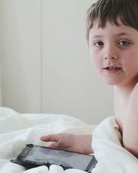 Close-up portrait of shirtless boy using digital tablet on bed