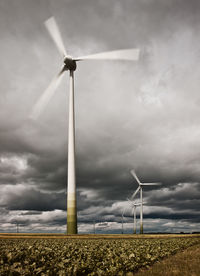 Wind turbines on field against cloudy sky